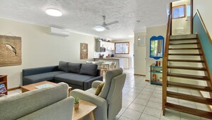 A living room with a sofa, armchair, and a small table. There is a staircase leading to an upper level. - Island Magic Townhouse 5 (Arcadia)