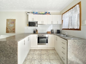 A modern kitchen with white cabinets, a built-in oven, a microwave, and a coffee maker.