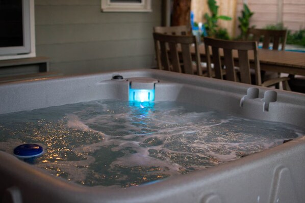 A hot tub with a blue light, surrounded by wooden chairs and a table.