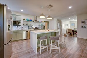 A modern kitchen with a central island, bar stools, and a dining area with a table and chairs.