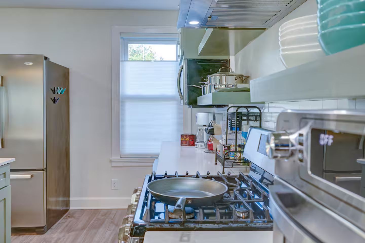 A kitchen with a stainless steel refrigerator, a gas stove, and a window with blinds.