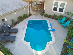 A rectangular swimming pool with a built-in hot tub, surrounded by lounge chairs and a covered patio area.