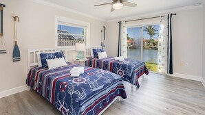 Un dormitorio con dos camas, un ventilador de techo, una ventana y vistas a una piscina.