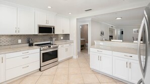 Una cocina moderna con armarios blancos, un refrigerador de acero inoxidable, un microondas y un horno.