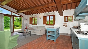 A room with a wooden ceiling, a sofa, a table, and a kitchen area with cabinets and a stove. - Francigena 6, Castelfiorentino, Italy (Castelfiorentino)
