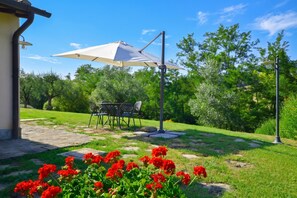 A patio area with a table and chairs, a white umbrella, and red flowers. - Francigena 6, Castelfiorentino, Italy (Castelfiorentino)