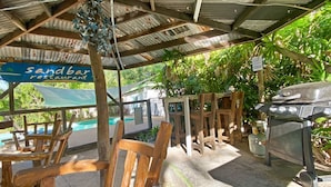 A covered outdoor seating area with wooden chairs and a barbecue grill. - The Barracks Arcadia 2 (Arcadia)