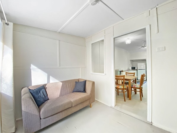 A room with a sofa, a dining table with chairs, and a kitchen area visible through an open door.
