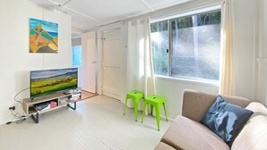 A modern living room with a flat-screen TV, a sofa, two green stools, and a painting on the wall. - The Barracks Arcadia 2 (Arcadia)