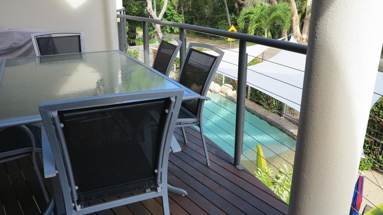 A glass-top table with chairs on a balcony overlooking a pool.
