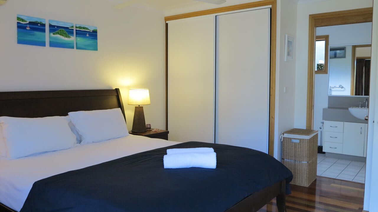 A hotel room with a bed, a nightstand with a lamp, a wardrobe, a bathroom with a sink and mirror, and artwork on the wall.