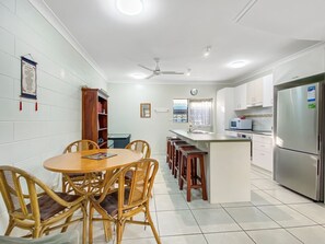 A modern kitchen with a dining area, white tiled walls, and a stainless steel refrigerator.