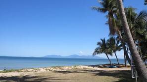 A beach with palm trees, a clear sky, and mountains in the distance. - Paradise Apartments 2 (Nelly Bay)