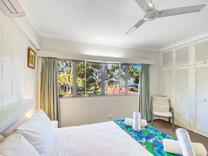 Une chambre d’hôtel avec un lit, une chaise, une fenêtre avec des rideaux et un ventilateur de plafond.
