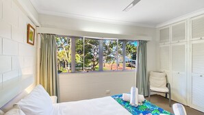 A hotel room with a bed, a chair, a window with curtains, and a ceiling fan.