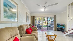 A living room with a sofa, a coffee table, a television, and a ceiling fan.