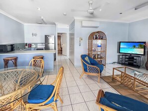 A modern living room with a TV, wicker furniture, and a kitchen area with a microwave. - Magnetic Shores Unit 2 (Arcadia)