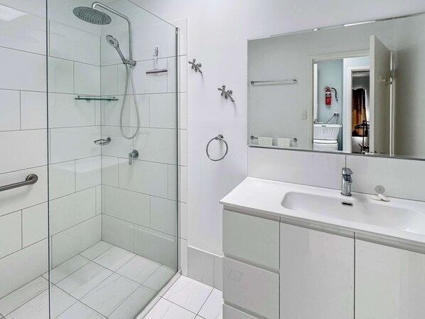 A modern bathroom with a glass-enclosed shower, a white sink, and a mirror reflecting the room. - Magnetic Shores Unit 2 (Arcadia)