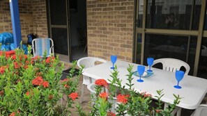 Eine Terrassenausstattung mit Esstisch, umgeben von roten Blüten und weißen Stühlen.