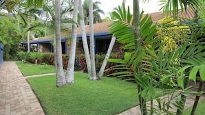 A well-maintained garden with palm trees, a brick pathway, and a building with a tiled roof. - Magnetic Shores Unit 2 (Arcadia)