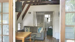 A room with a wooden table, a sofa with cushions, a door, and a window. - Picnic Bay Chalet Unit 2 (Picnic Bay)