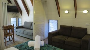 A room with a bed, two sofas, a TV, and a window with blinds.