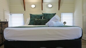 A neatly made bed with green patterned pillows, a white comforter, and a rolled towel. - Picnic Bay Chalet Unit 2 (Picnic Bay)