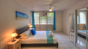 Habitación de hotel con cama, mesita de noche, ventilador de techo, ventana con cortinas y vista al exterior.