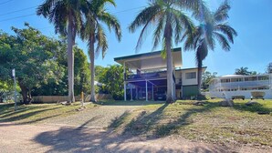 A two-story building with a covered outdoor area, palm trees, and a clear sky.