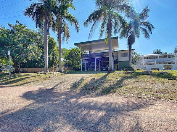 A two-story building with a covered outdoor area, palm trees, and a clear sky.