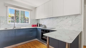 A modern kitchen with marble countertops, a built-in oven, and a window with a view of trees.