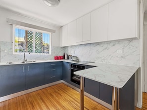 A modern kitchen with marble countertops, a built-in oven, and a window with a view of trees.