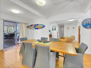 Een eetruimte met een houten tafel, grijs gestoffeerde stoelen, een decoratieve wandhanger en een klok.