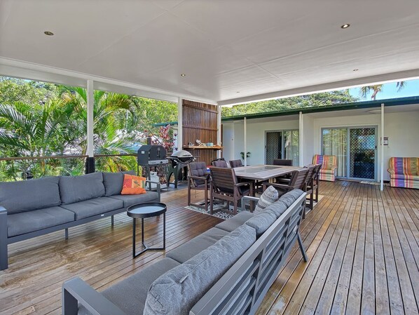Un espace de vie à aire ouverte avec une terrasse en bois, un ensemble de canapés, une table à manger et un barbecue.