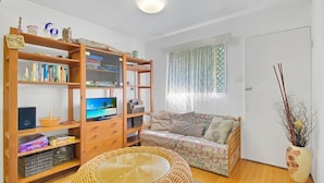 A cozy living room with a television, bookshelf, sofa, and a wicker coffee table.
