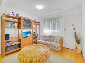 A cozy living room with a television, bookshelf, sofa, and a wicker coffee table.