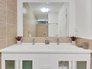 A bathroom with a double sink, a large mirror, and two potted plants.