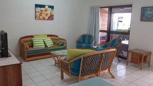 A living room with a colorful sofa, wicker chairs, a small table, and a television on a stand. - Magnetic Shores Unit 3 (Arcadia)