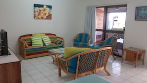 Ein Wohnzimmer mit einem farbenfrohen Sofa, Korbstühlen, einem kleinen Tisch und einem Fernseher auf einem Lowboard.