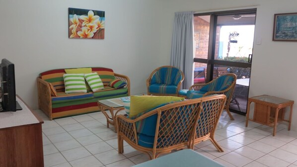 A living room with a colorful sofa, wicker chairs, a small table, and a television on a stand.