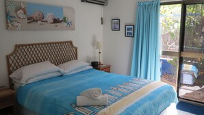 A bedroom with a bed, a nightstand, a lamp, a window with curtains, and a wall with framed pictures. - Magnetic Shores Unit 3 (Arcadia)