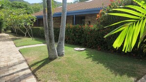 A house with a tiled roof, a paved pathway, and a well-maintained lawn with palm trees and flowering bushes. - Magnetic Shores Unit 3 (Arcadia)