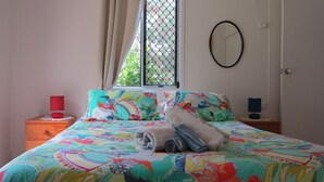 Ein Bett mit einer farbenfrohen Steude, einer roten Lampe, einem Fenster mit Blick auf Grünflächen und einem runden Spiegel an der Wand.