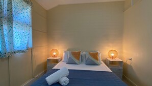 A hotel room with a bed, two bedside tables, and a window with a curtain. - The Captain's Manor On Cook 5 (Arcadia)