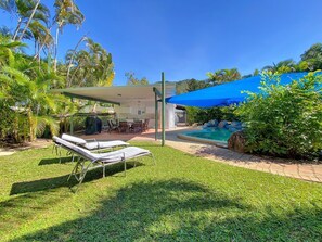 Un jardin avec une piscine, des chaises longues et un espace patio couvert.