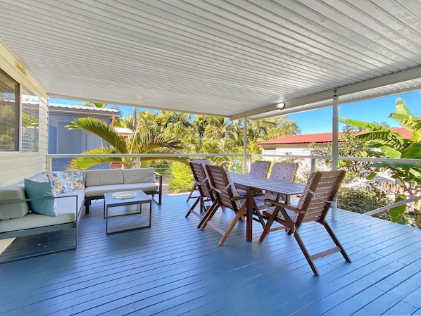 A covered outdoor deck with a sofa, dining table, and chairs.