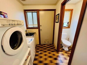 Une petite buanderie équipée d’un lave-linge, d’un évier et de toilettes.
