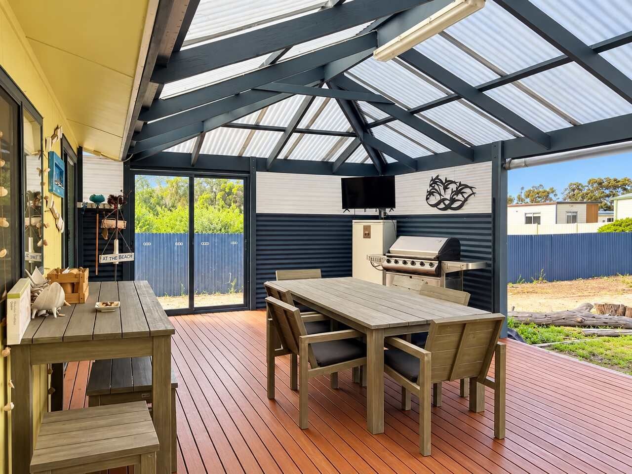 A covered outdoor area with a wooden table and chairs, a barbecue grill, and a view of the outdoors.