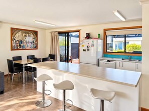 Une cuisine moderne avec un îlot central, des tabourets de bar, une table à manger avec des chaises et une vue par la fenêtre.