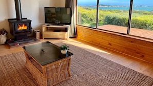 A living room with a fireplace, a television, a large window with a view, and a wooden floor. - C4 Miles - Wood Fire - Sea Views - RC/AC (Robe)